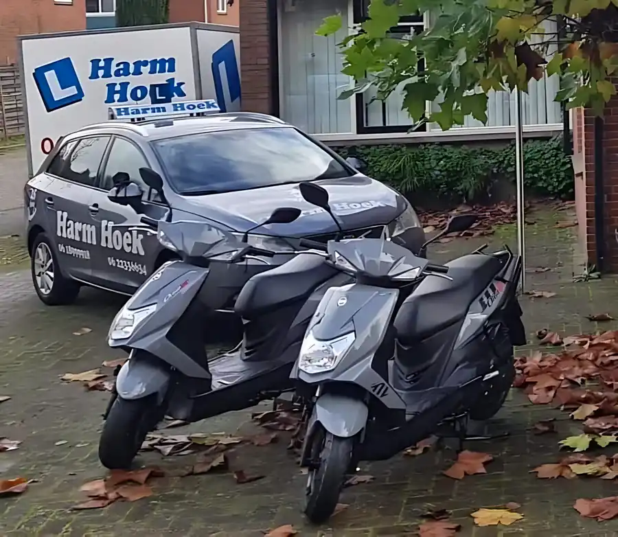 Twee lesbromfietsen en de lesauto van Rijschool Harm Hoek voor het pand in Borne